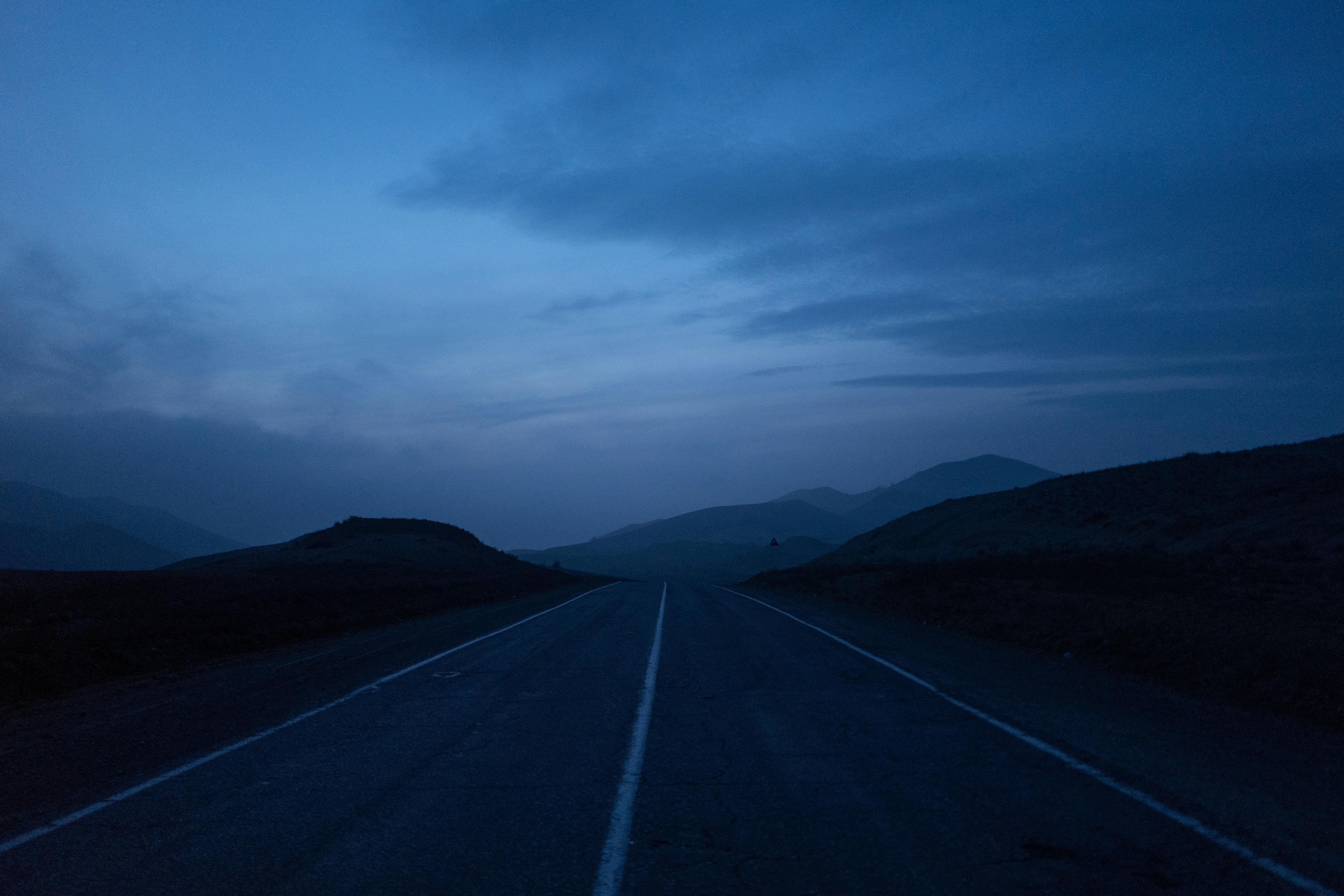 A night road cutting through a dark plain under heavy clouds